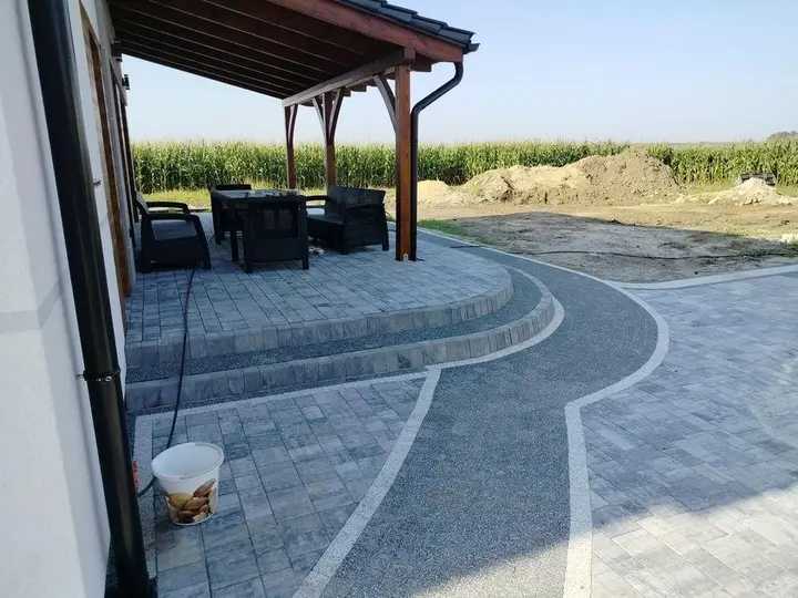 Taras z kostki brukowej pod pergolą z łukiem ze żwiru ozdobnego